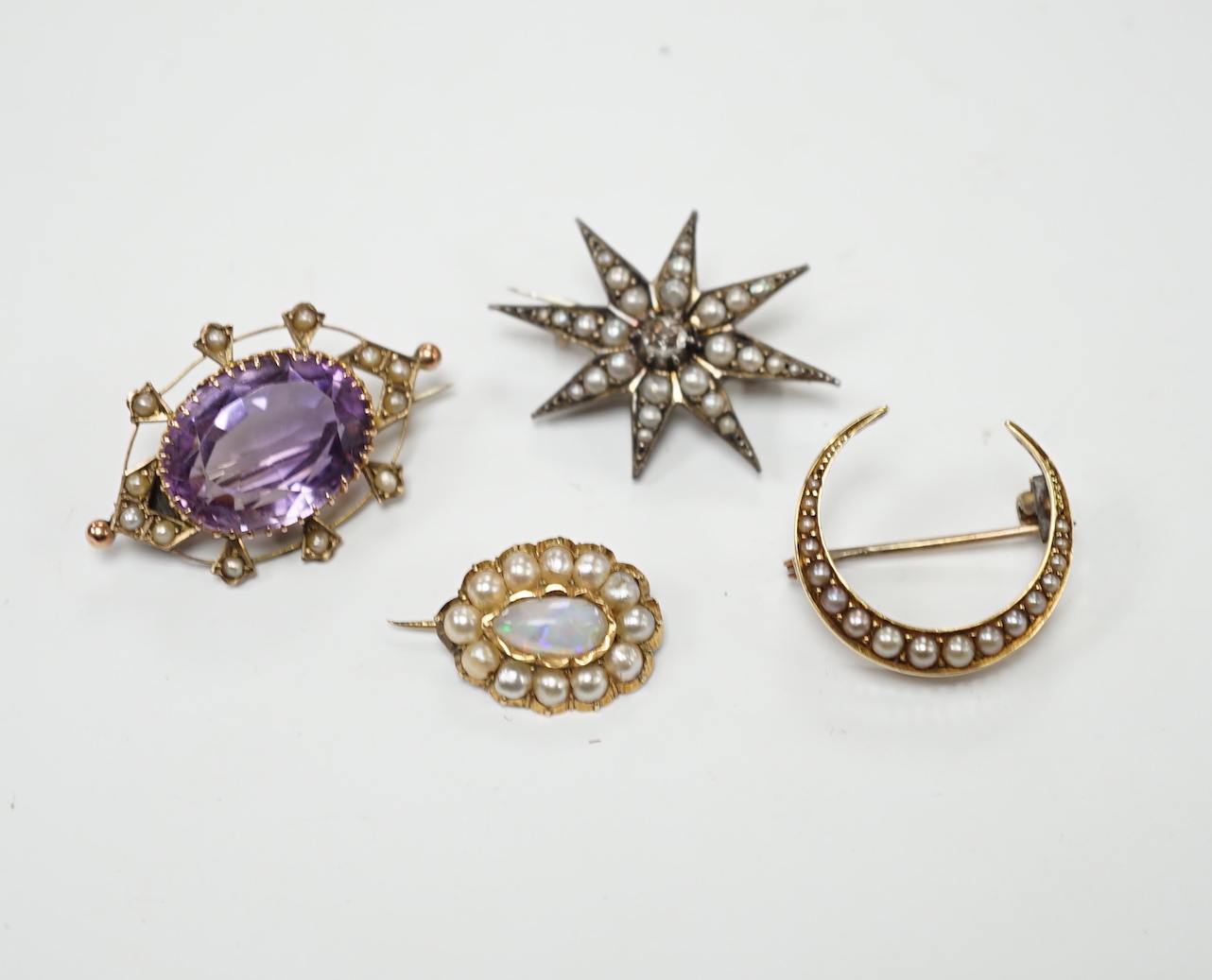 An early 20th century 9ct, amethyst and seed pearl set oval brooch, 33mm, a yellow metal and seed pearl set crescent brooch, a yellow metal, opal and split pearl set brooch and a rose cut diamond and split pearl set star